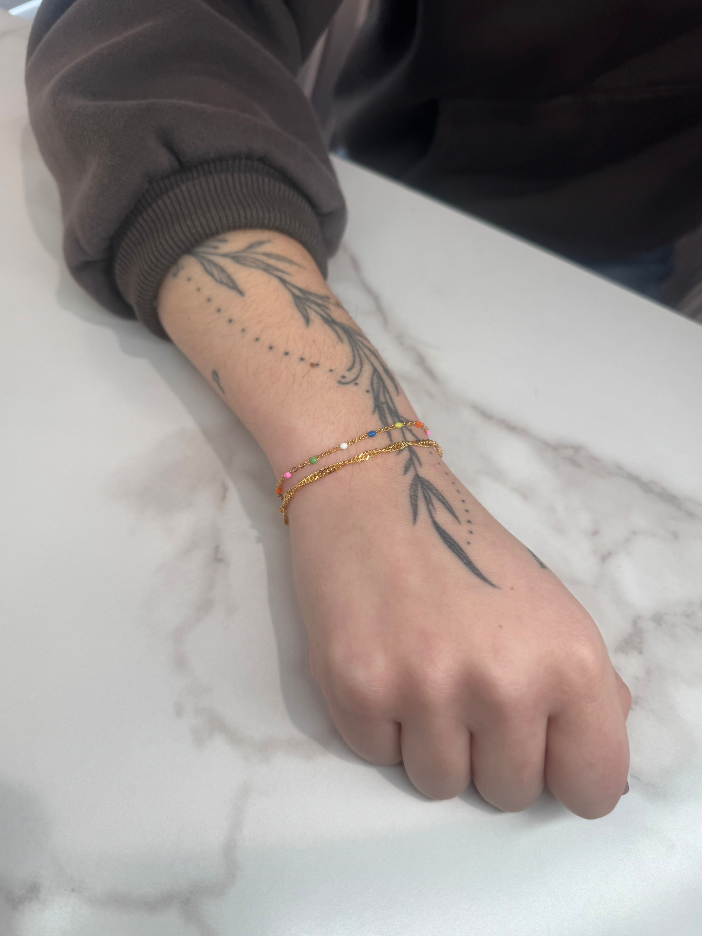 Two delicate gold permanent bracelets on a tattooed wrist