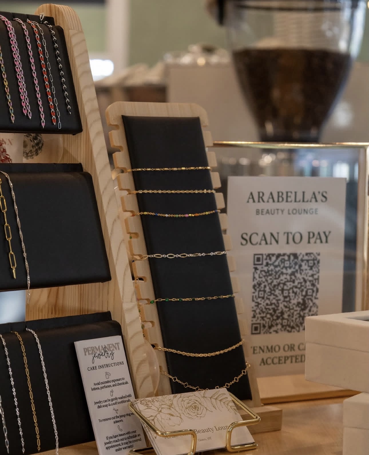 Permanent jewelry display with gold chains, silver chains, and a scan-to-pay sign at Arabella's Beauty Lounge